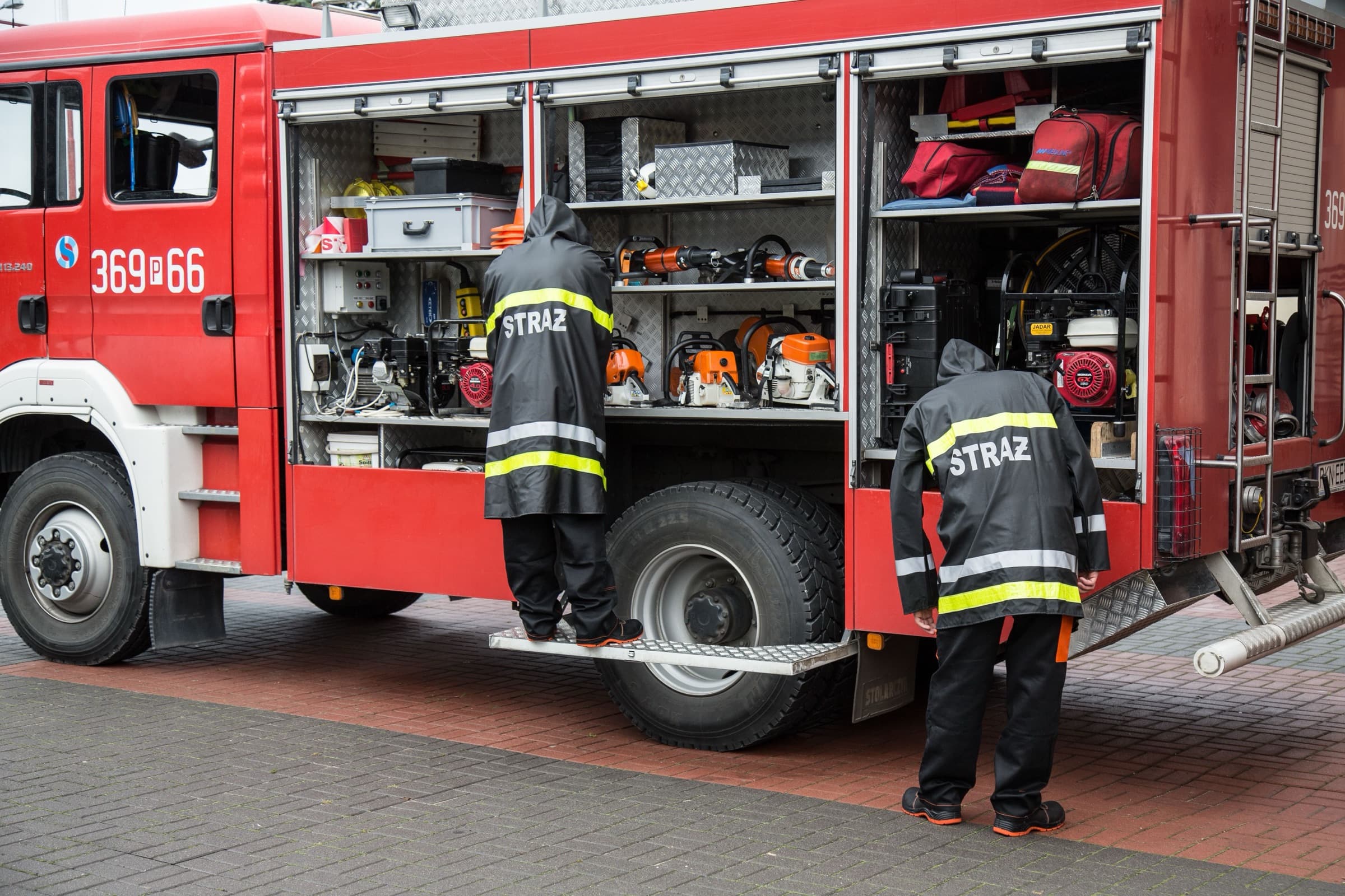 Strażacy przygotowujący sprzęt w otwartych skrytkach wozu strażackiego