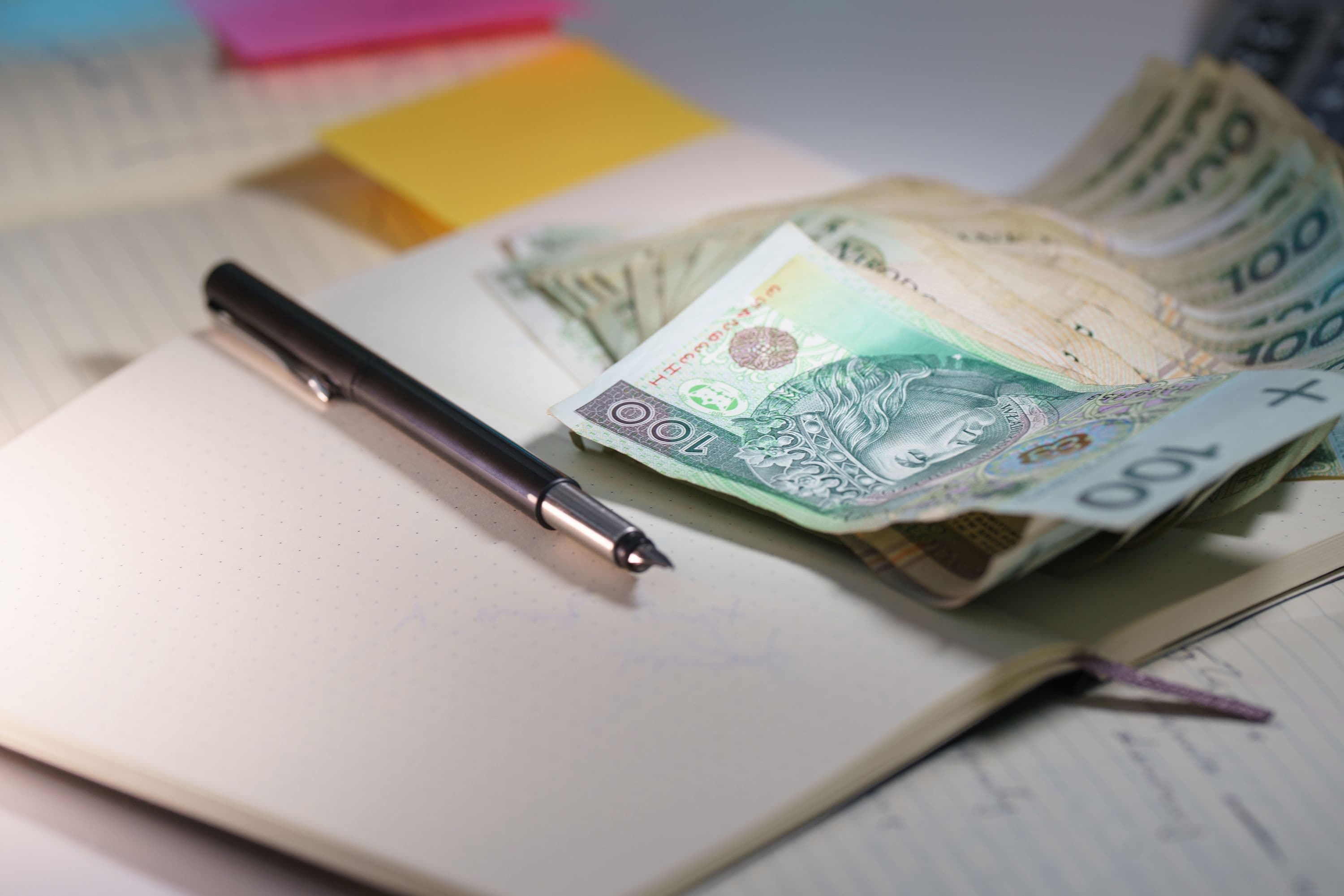 Banknoty 100 zł na otwartym notesie z piórem — planowanie budżetu na stację ładowania i montaż