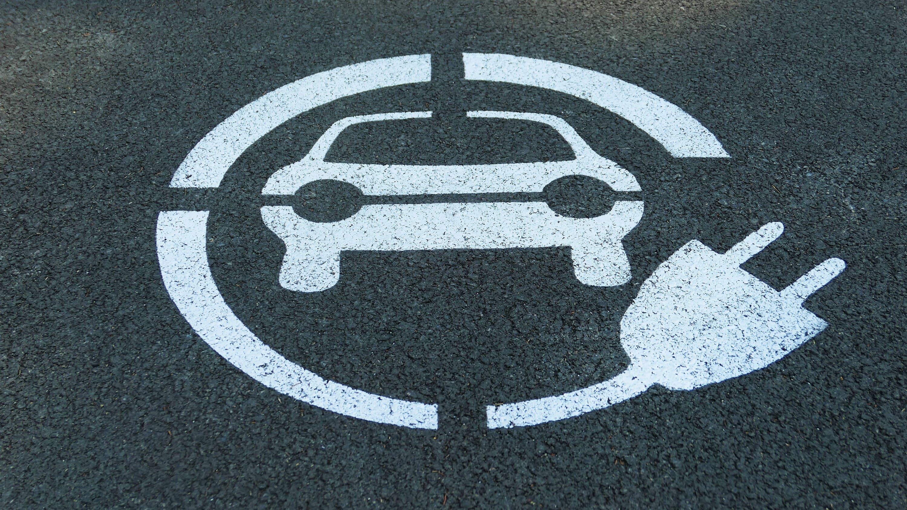 Symbol samochodu elektrycznego z wtyczką namalowany na asfalcie miejsca do ładowania na parkingu