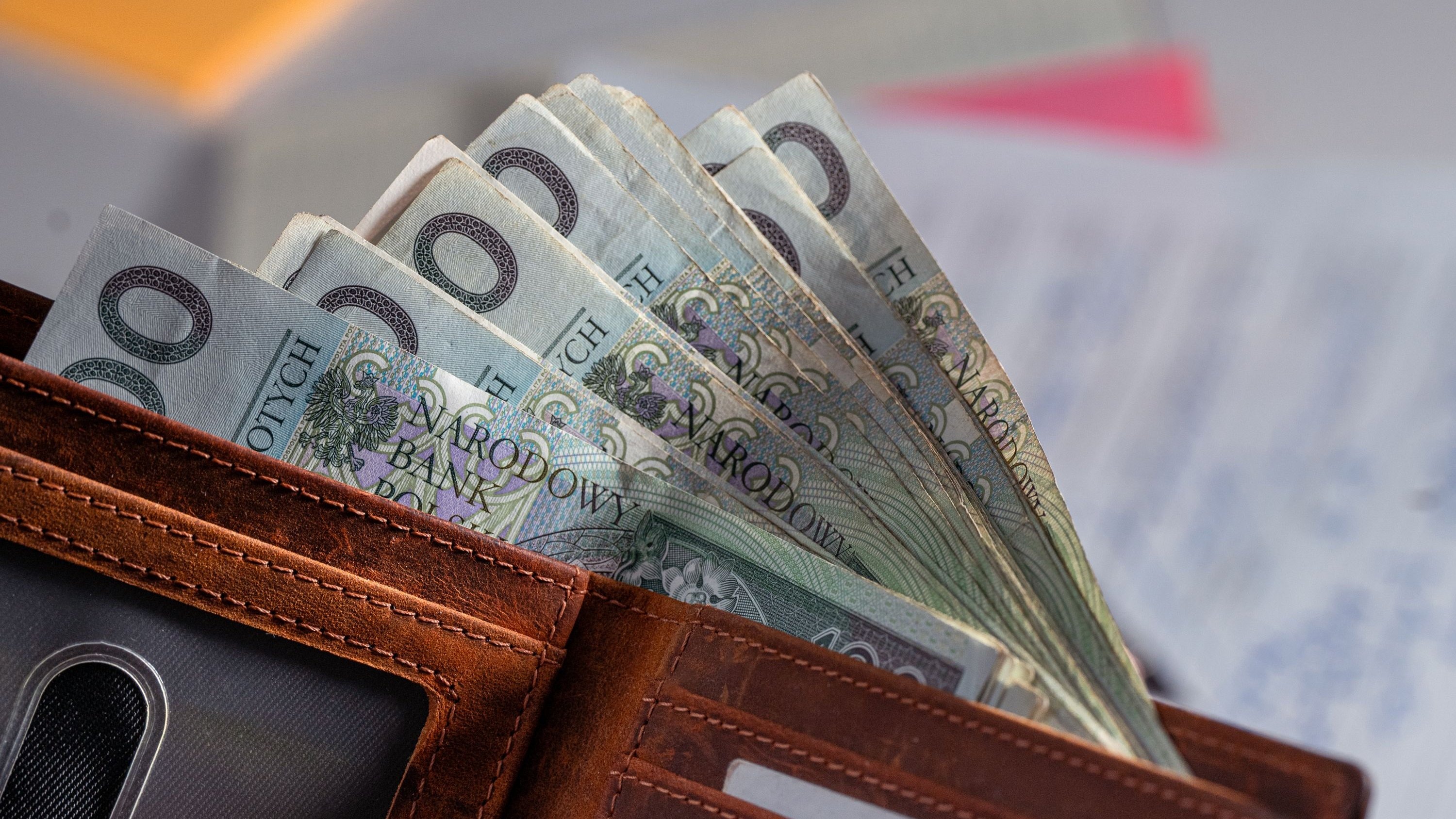 Portfel z banknotami 100 zł — koszt ładowania auta elektrycznego w porównaniu z tankowaniem