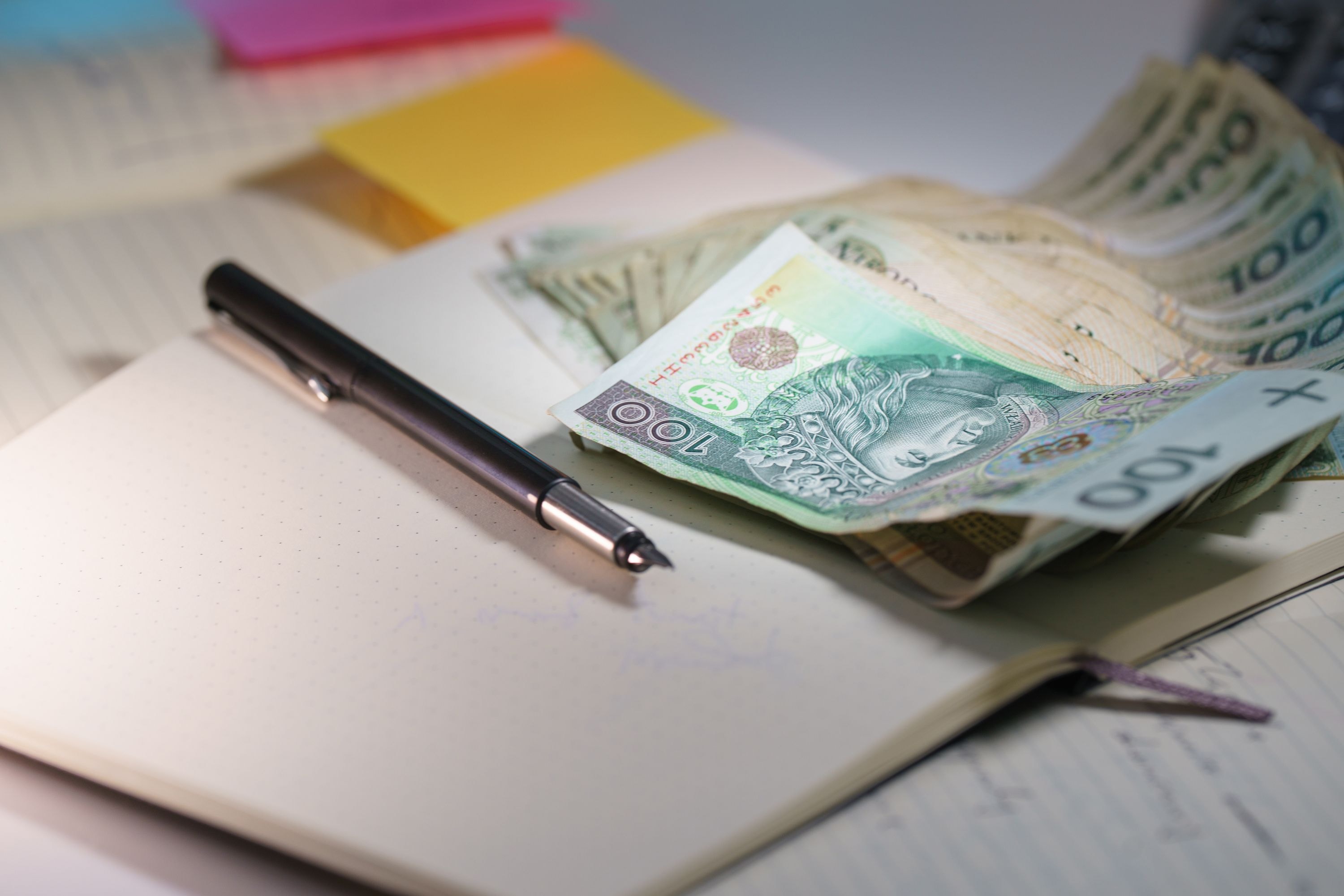 Banknoty 100 zł na otwartym notesie z piórem — planowanie budżetu na stację ładowania i montaż