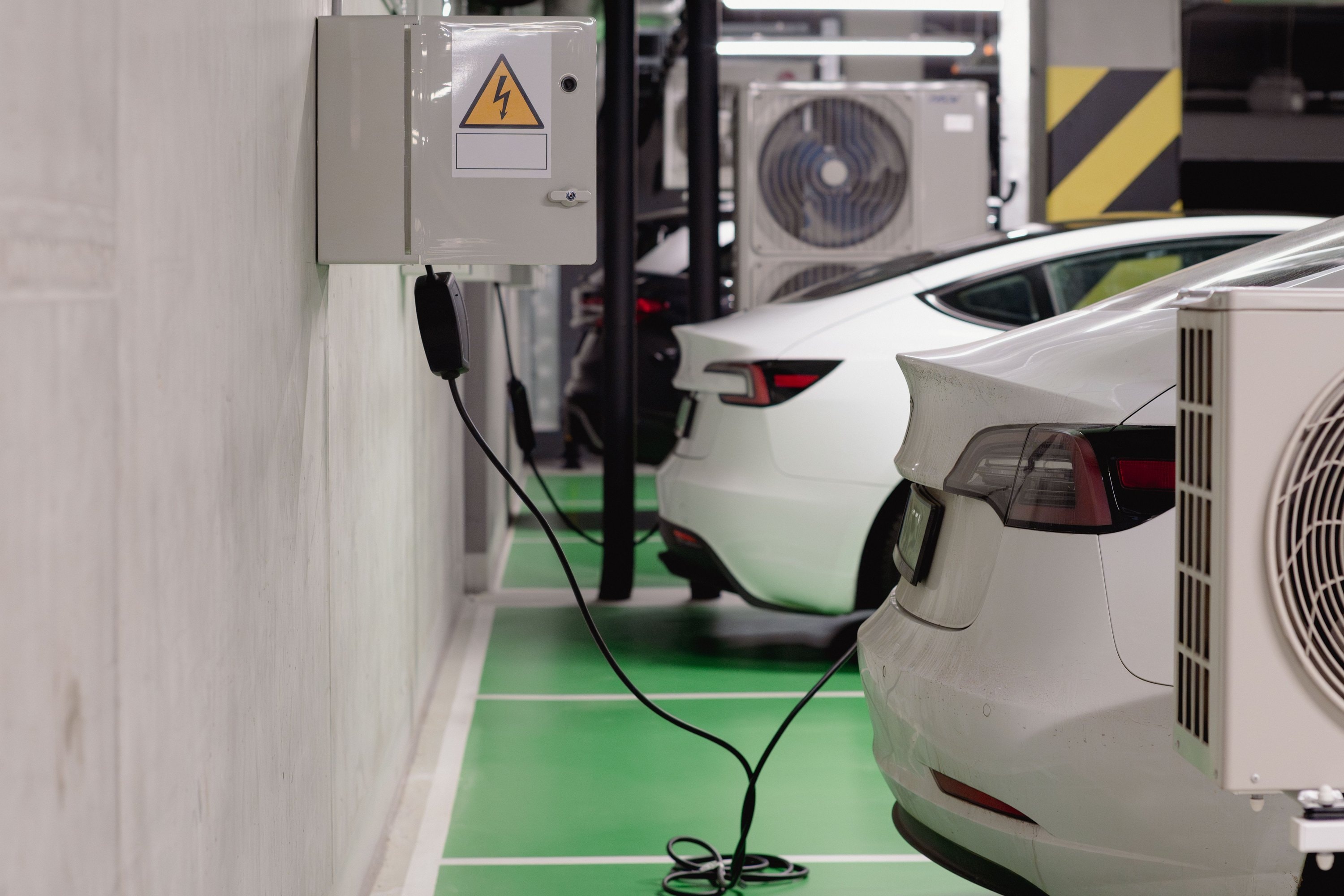 Samochody elektryczne ładowane w garażu podziemnym z ładowarek przy rozdzielnicy elektrycznej